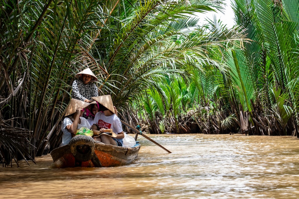 Gäste im Ruderboot durch die Palmenkanäle des Mekong-Deltas