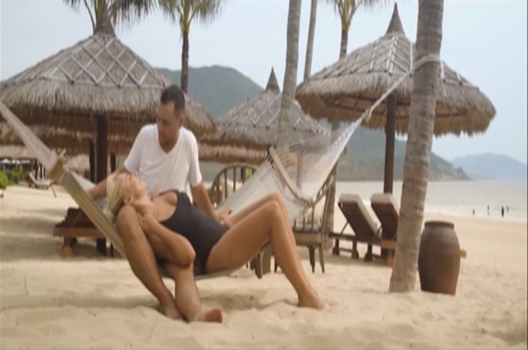 Paar in der Hängematte unter Palmschirmen am Strand des Resorts